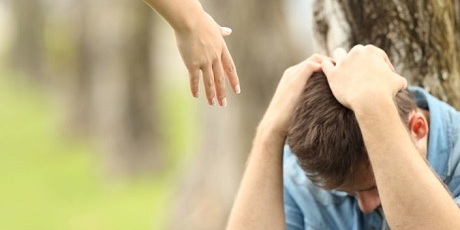 Sad teen sitting on the grass in a park and a woman hand offering help with a green background